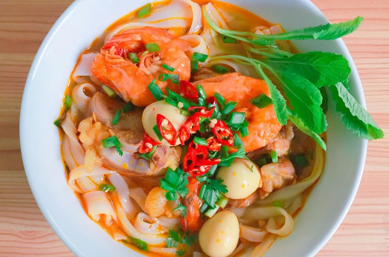 A vibrant bowl of Vietnamese noodle soup with shrimp, herbs, and quail eggs.